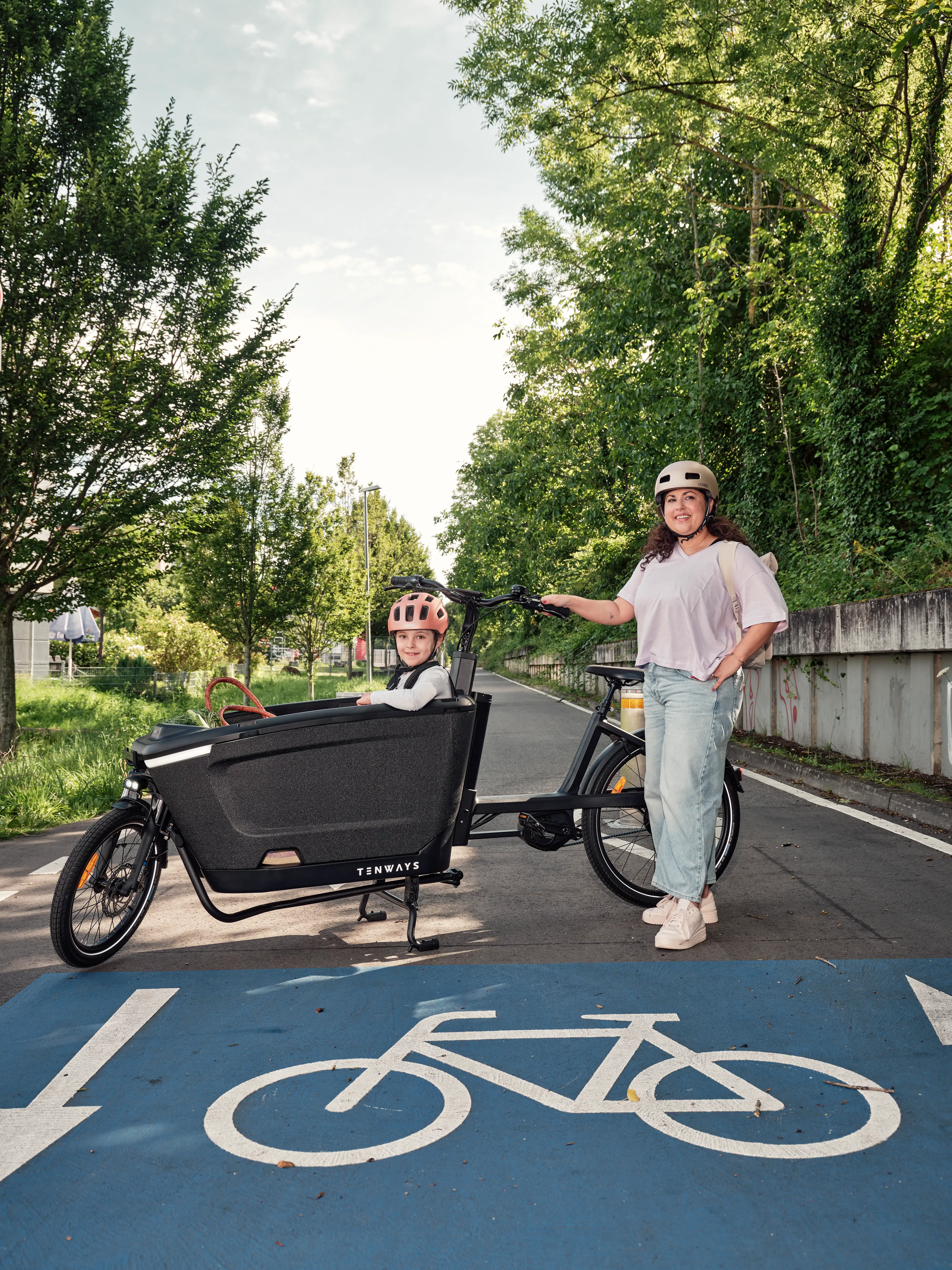 JobRadlerin posiert stolz neben ihrem Lastenrad mit Kind auf der Fahrradstraße JobRadlerin posiert stolz neben ihrem Lastenrad mit Kind auf der Fahrradstraße